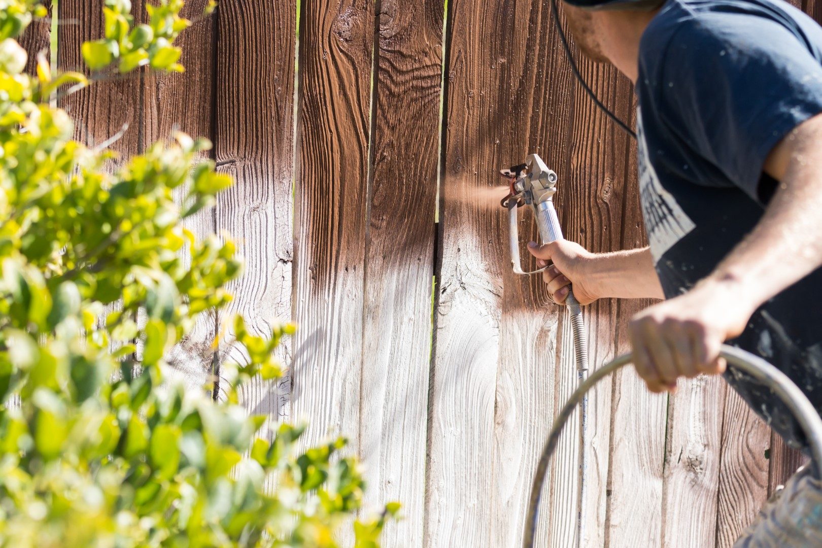 Professional Painter Spraying House Yard Fence with Wood Stain.